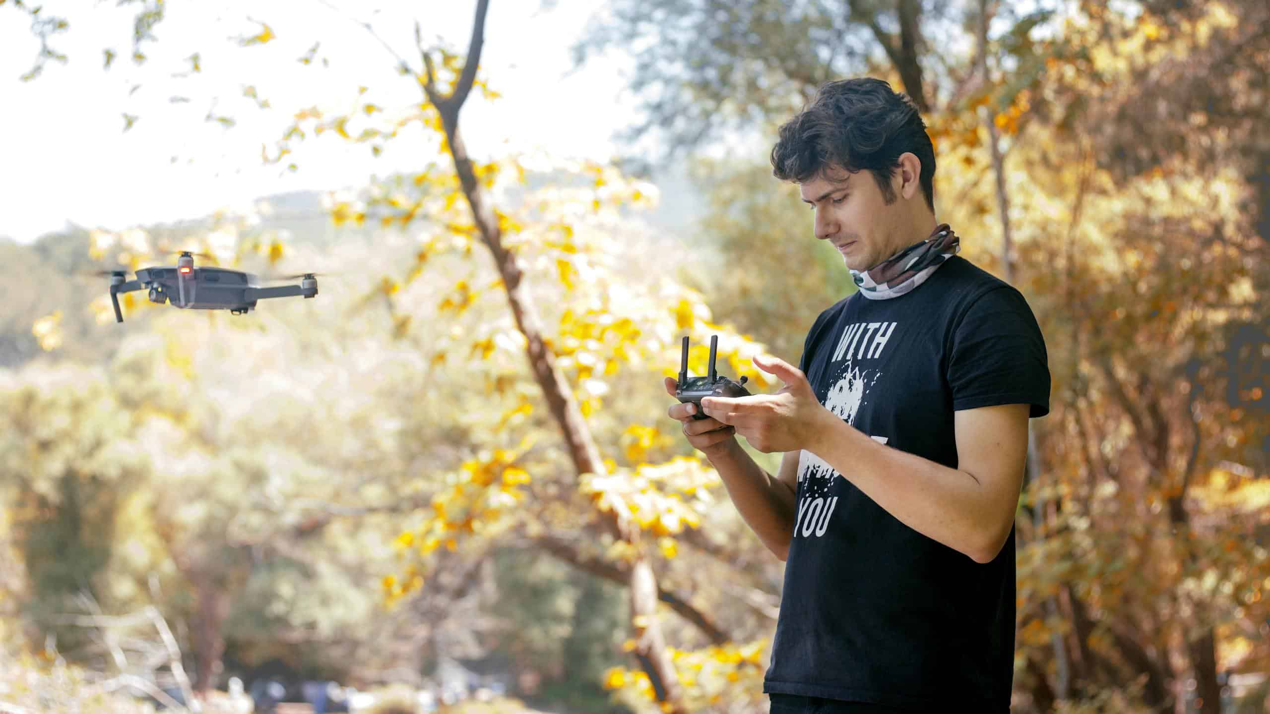 A young man controls a drone in a vibrant autumn park, capturing scenic views.
