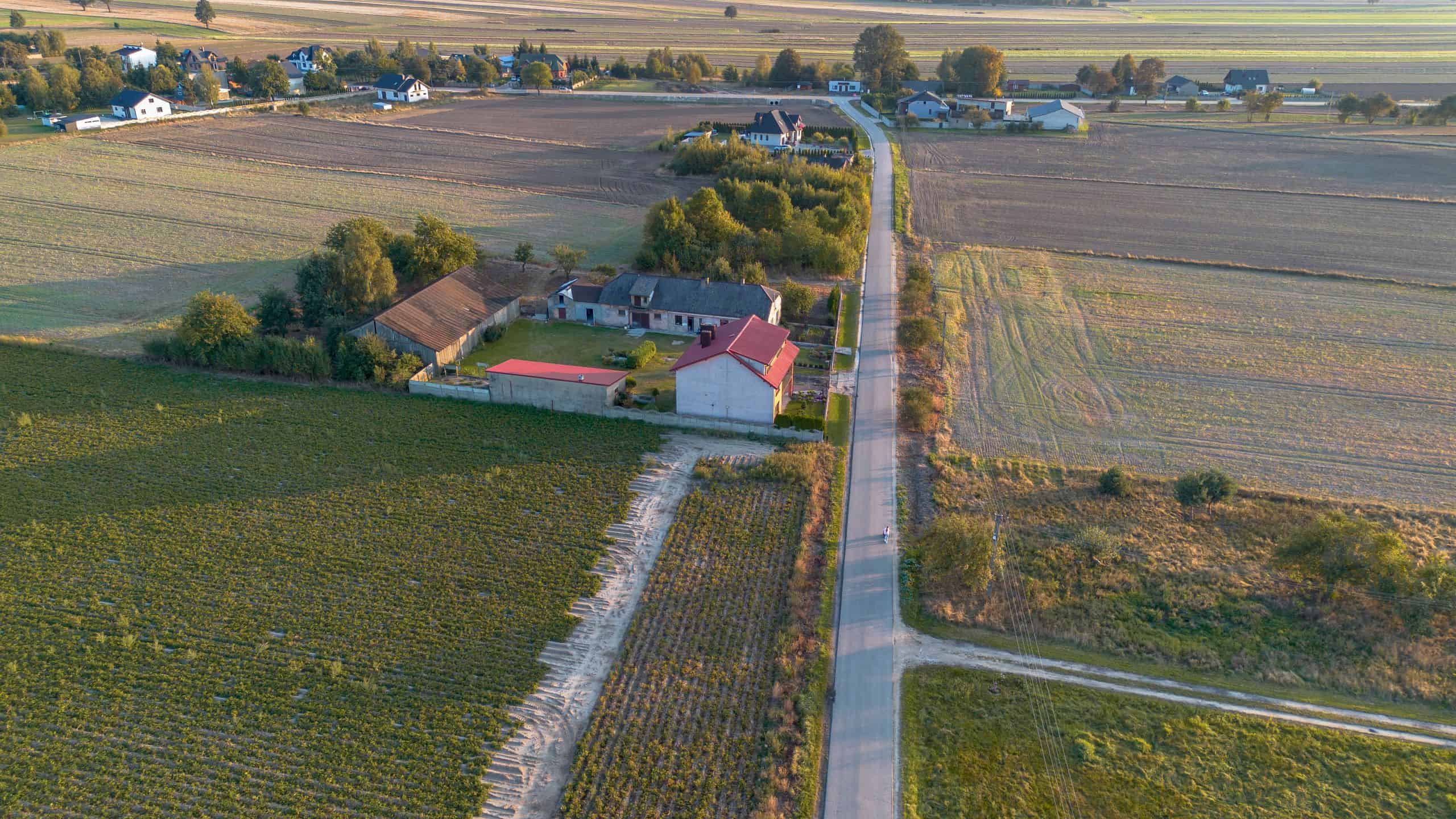 Zdjęcie z drona ukazujące pola, drogi i zabudowania na wsi.